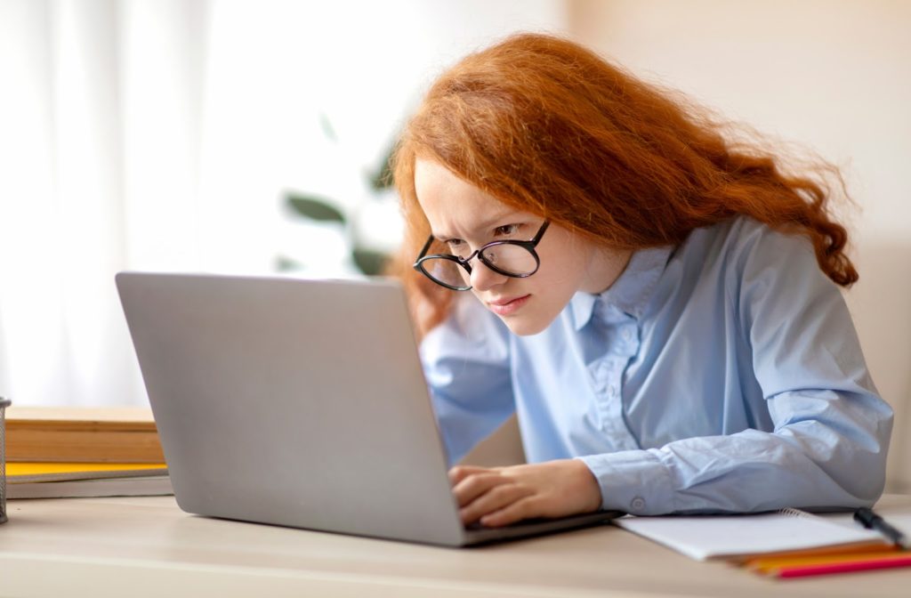 Young girl sitting close to her laptop screen due to poor vision.