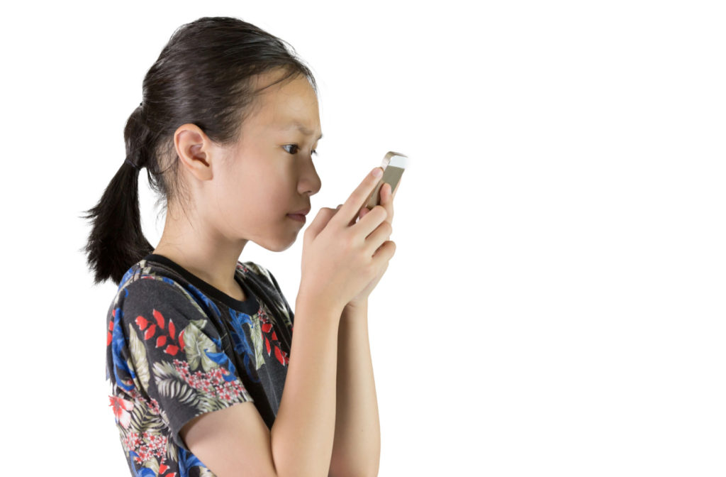 A young girl is using her mobile phone closely to her face.