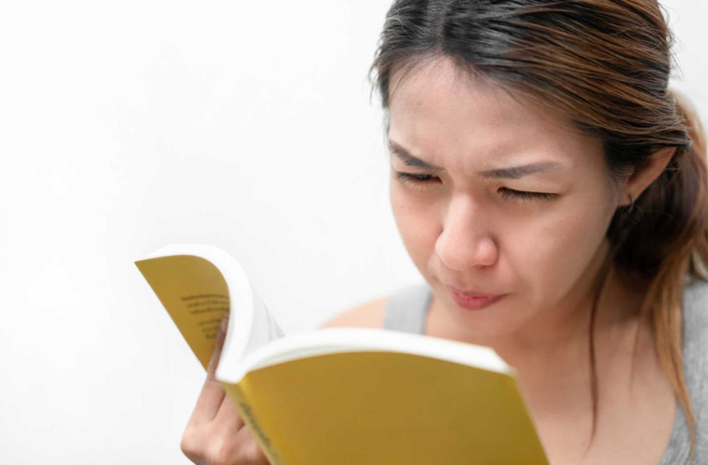 A woman having trouble reading the book due irritation on the eye because of dry eyes.