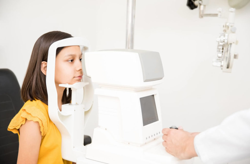 A young girl is looking through into an auto refractometer while sitting on a chair