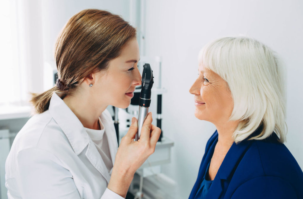 A female optician is using an ophthalmoscope while examining the eye of a female patient