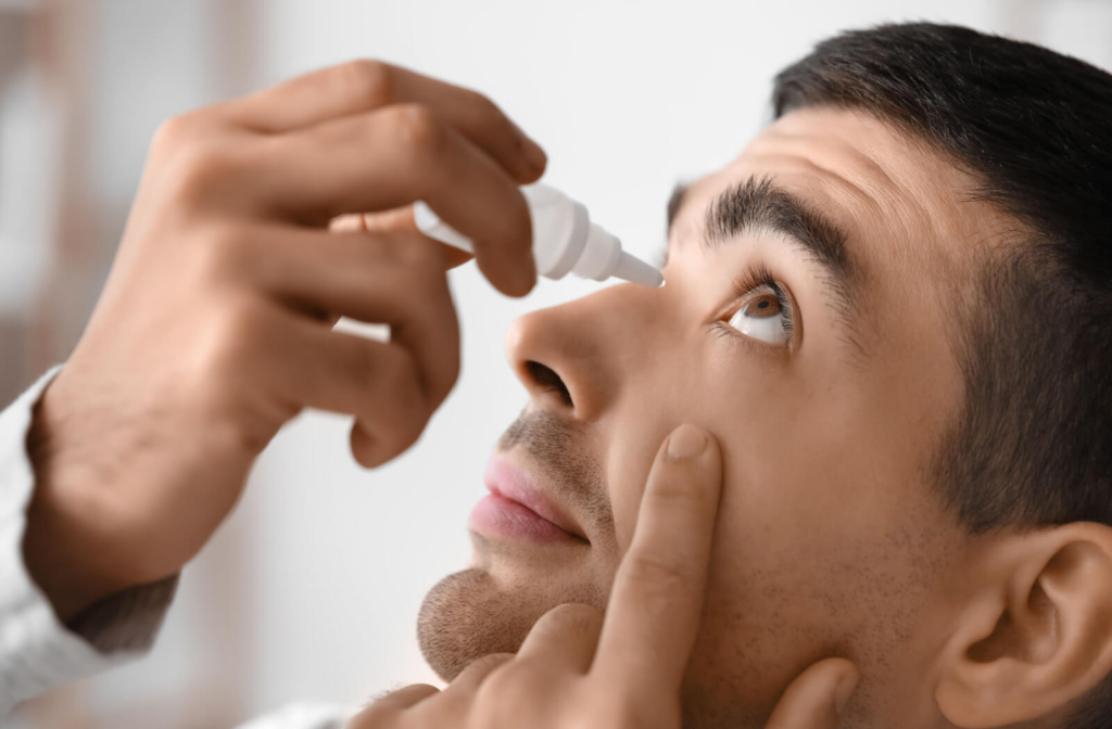 A young man looking up and pulling his lower eyelid down, about to put eye drops in his left eye.