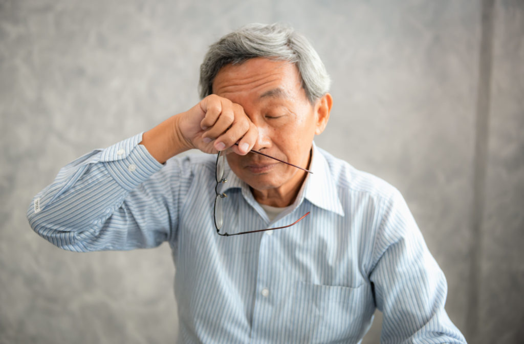 A senior man holding his glasses and rubbing his right eye with his right hand.