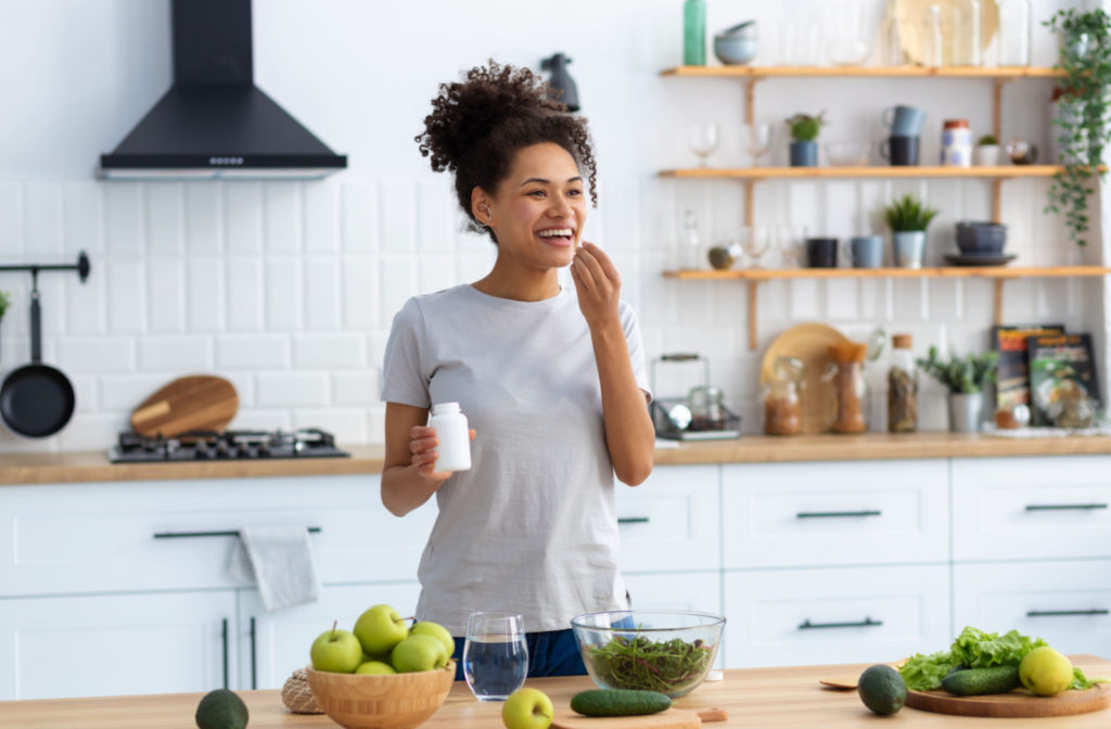 A woman with curly hair taking her vitamins in a brightly lit kitchen.