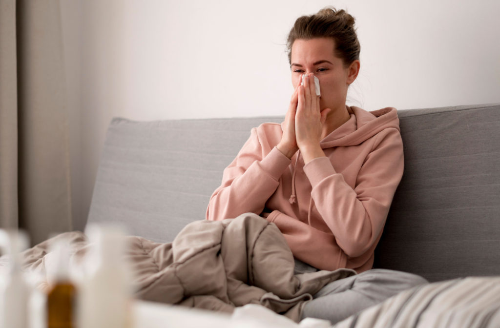 A sickly-looking young woman in a cozy hoody suffering from a runny nose caused by her allergies.