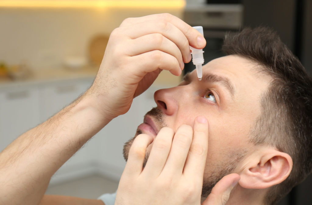 A young man applying eye drops to his left eye.