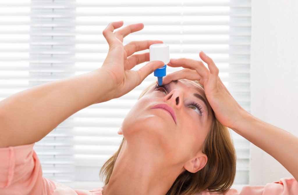 A woman applying a drop of atropine eyedrops on her right eye.