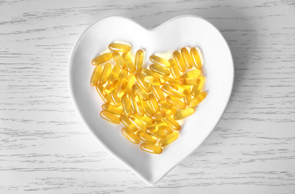 A heart-shaped bowl containing omega-3 supplement capsules.