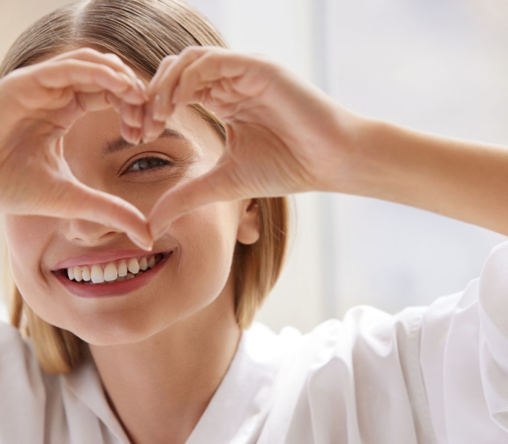 Woman smiling while forming a heart shape with her hands near her eyes, symbolizing care for eye health and vision.
