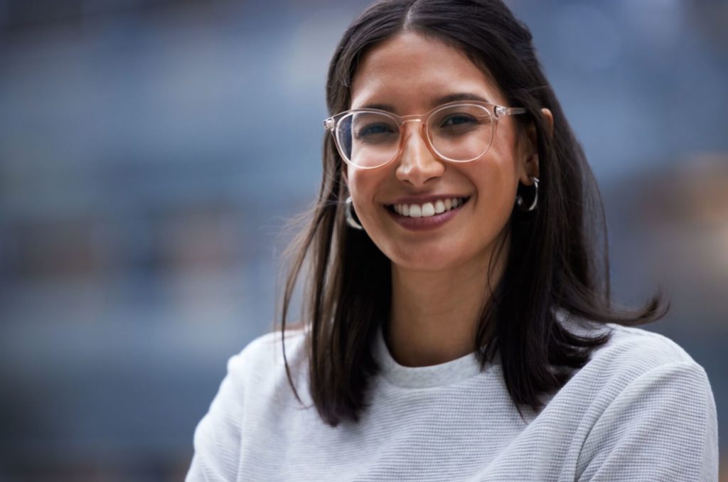 A smiling young person wearing clear frames with corrective lenses.