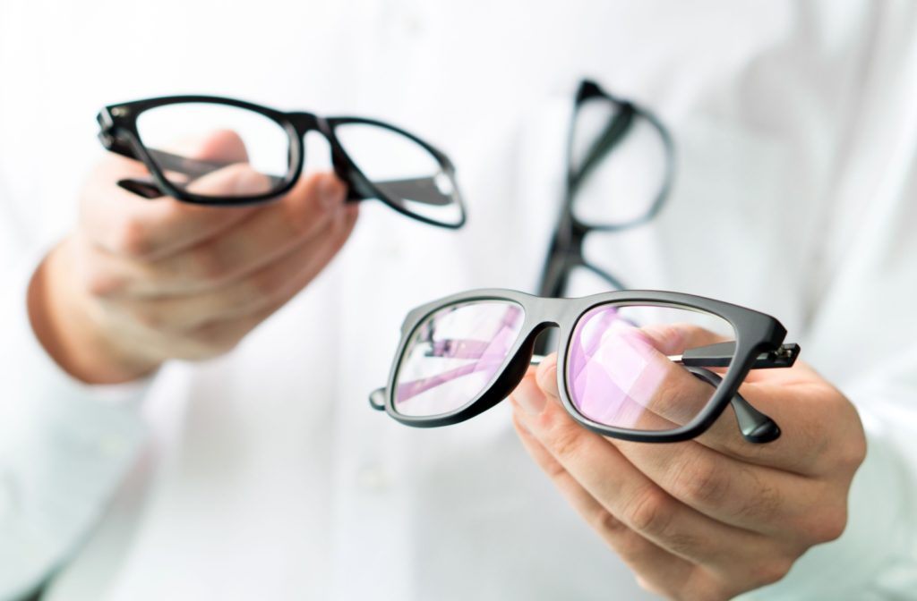 An optometrist holds out two different pairs of prescription glasses to compare.