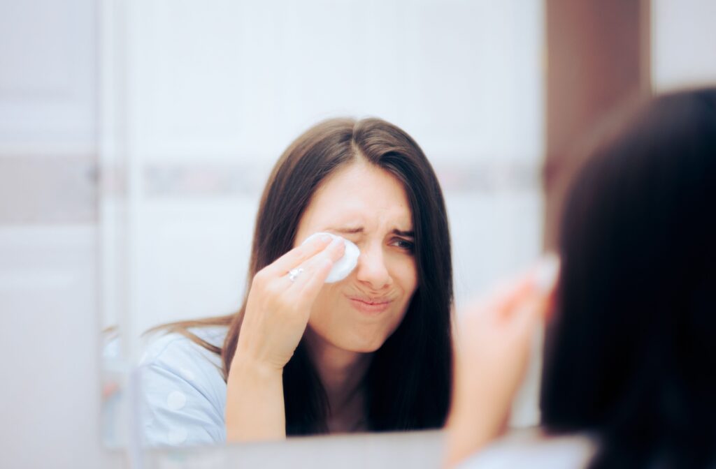 A young adult grimaces while cleaning their eyes in an attempt to relieve discomfort from improperly fitted contact lenses