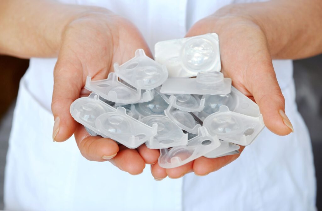 Hands holding a pile of expired disposable contact lens blister packs.