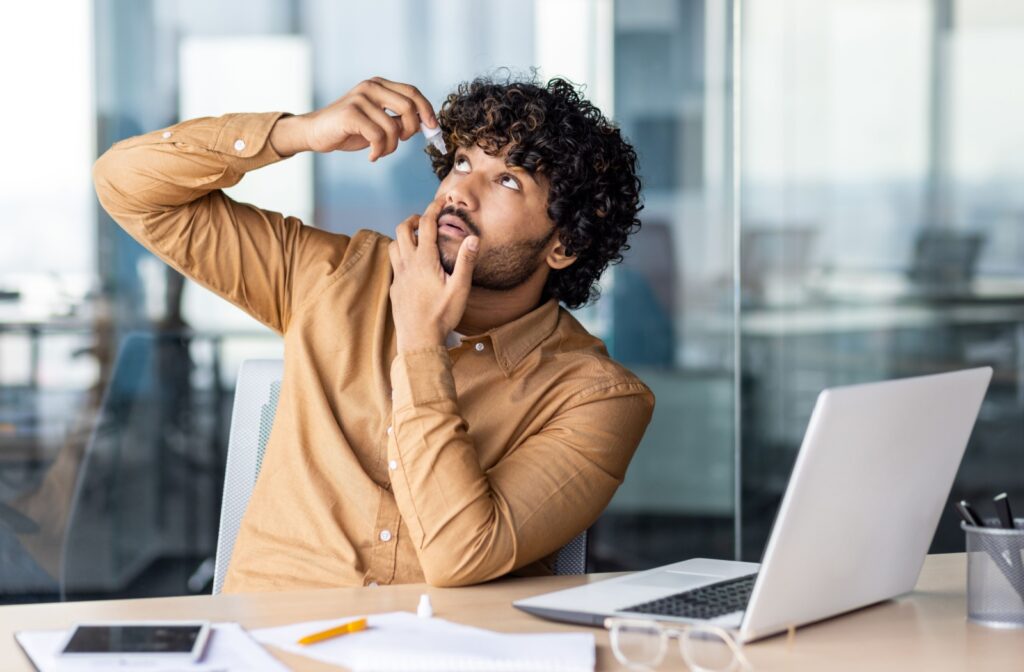 A person using artificial tears while taking a break from computer work to manage dry eye symptoms.
