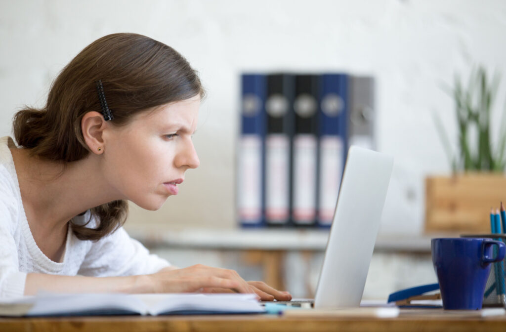 A person squinting, struggling to see what's on the laptop screen in front of them.